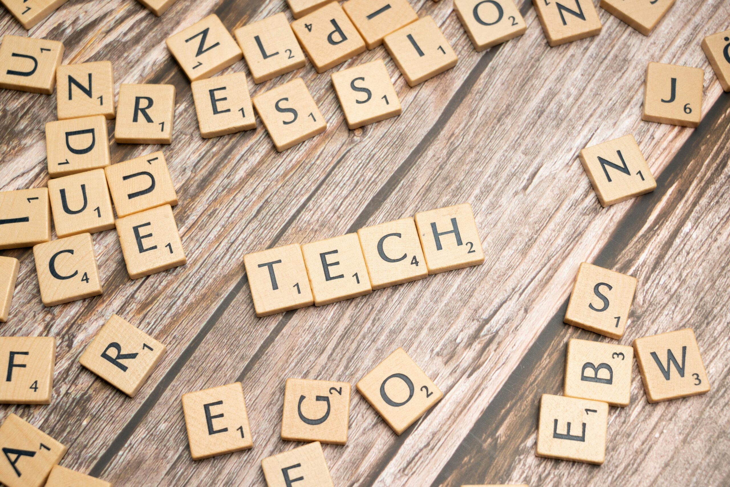 Wooden Scrabble tiles spelling 'TECH' on a textured surface, showcasing creativity.